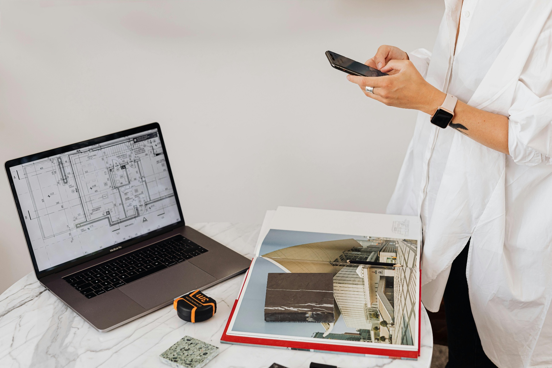 Designer reviewing construction blueprints on a laptop while checking their phone